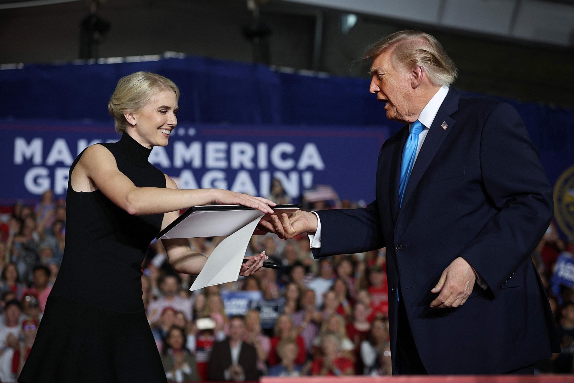 El presidente Donald Trump le devuelve a su asistente Natalie Harp una orden ejecutiva en un acto de campaña.