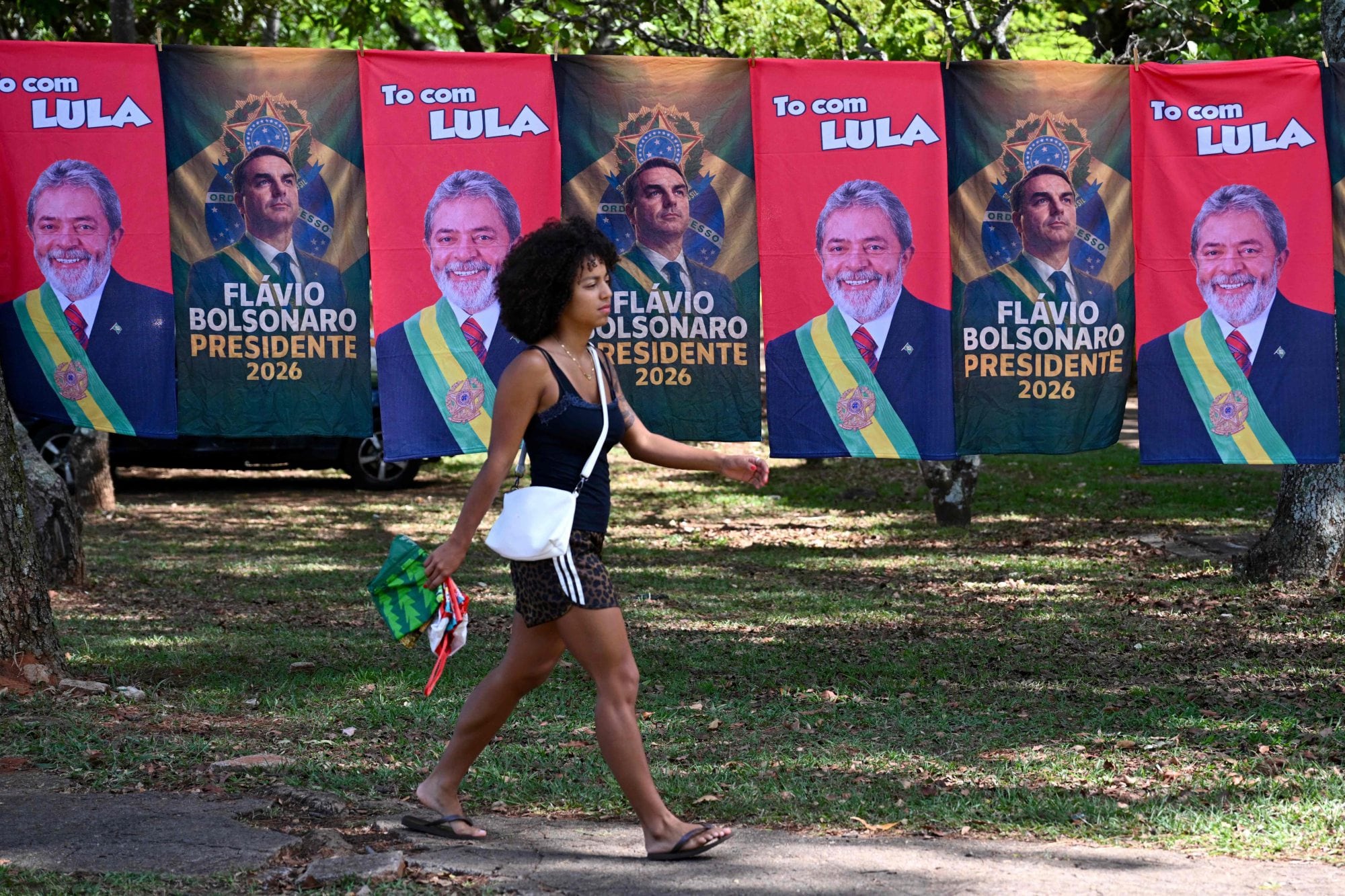 Elecciones en Brasil: Lula empata con Flavio Bolsonaro y recupera la aprobación de su gobierno a tres días del balotaje 8 Una mujer pasa junto a banderas y toallas que exhiben las imágenes del presidente de Brasil y candidato presidencial, Luiz Inácio Lula da Silva, y del senador de derecha y también candidato presidencial, Flavio Bolsonaro, en Brasilia