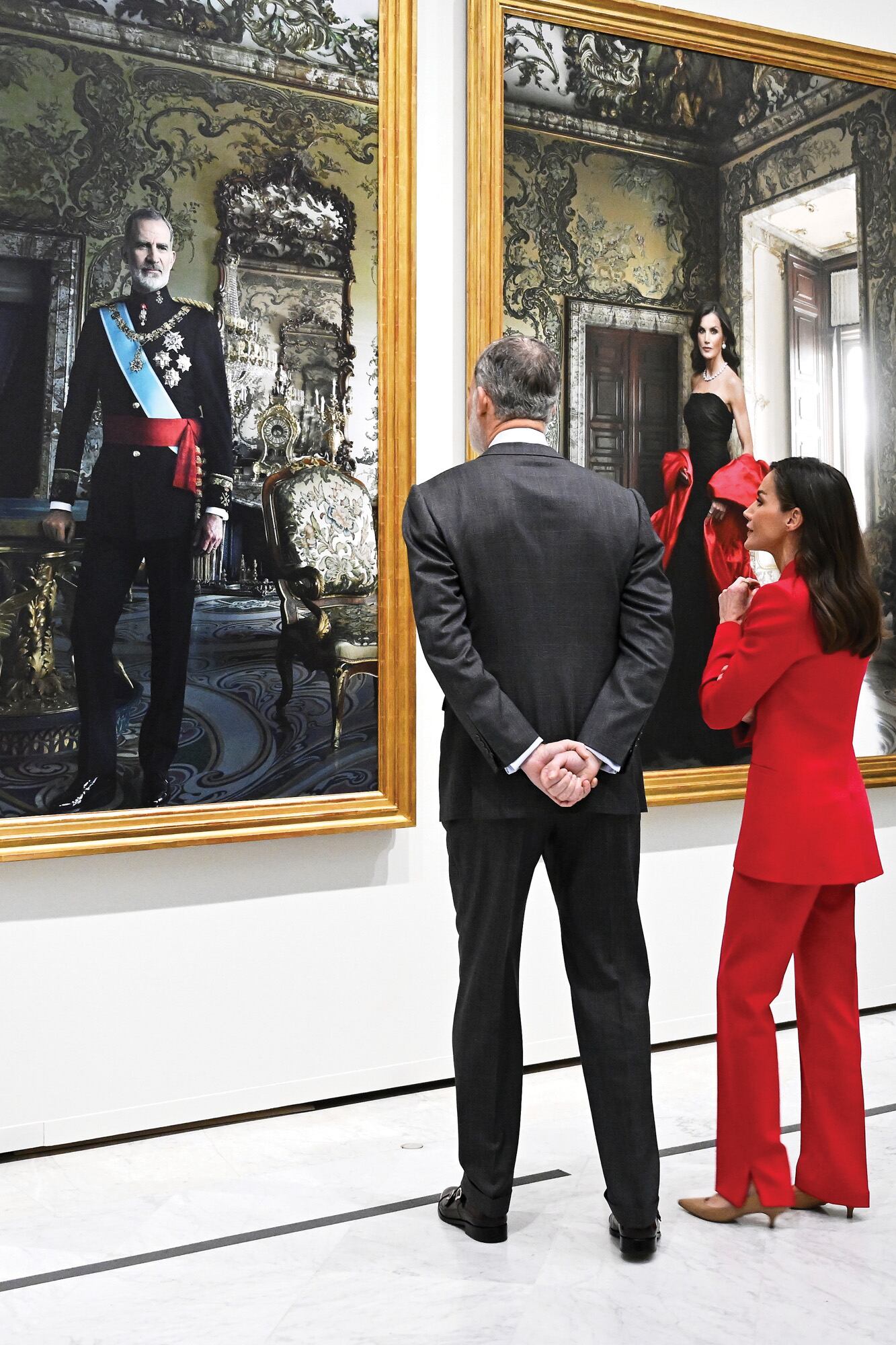 En la obra, el Rey luce su uniforme de capitán general del Ejército de Tierra- con diversas condecoraciones como el Toisón de Oro-, mientras que Letizia lleva un vestido negro de línea sirena en tul de seda plisado, con fourreau de faya de seda de Balenciaga que data de 1948. Completa el look, una capa de gala en seda tafetán de color rosa del mismo diseñador.