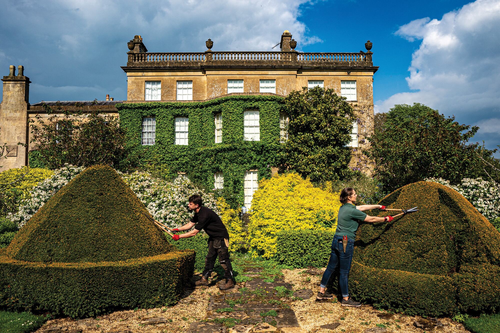 Dos jardineros trabajan con tijeras de podar los topiarios de Highgrove, la residencia personal de los reyes Carlos y Camilla (que se ve al fondo). La imagen es de mayo del año pasado, horas antes de que los jardines se abrieran al público para celebrar el Día Mundial del Topiario.