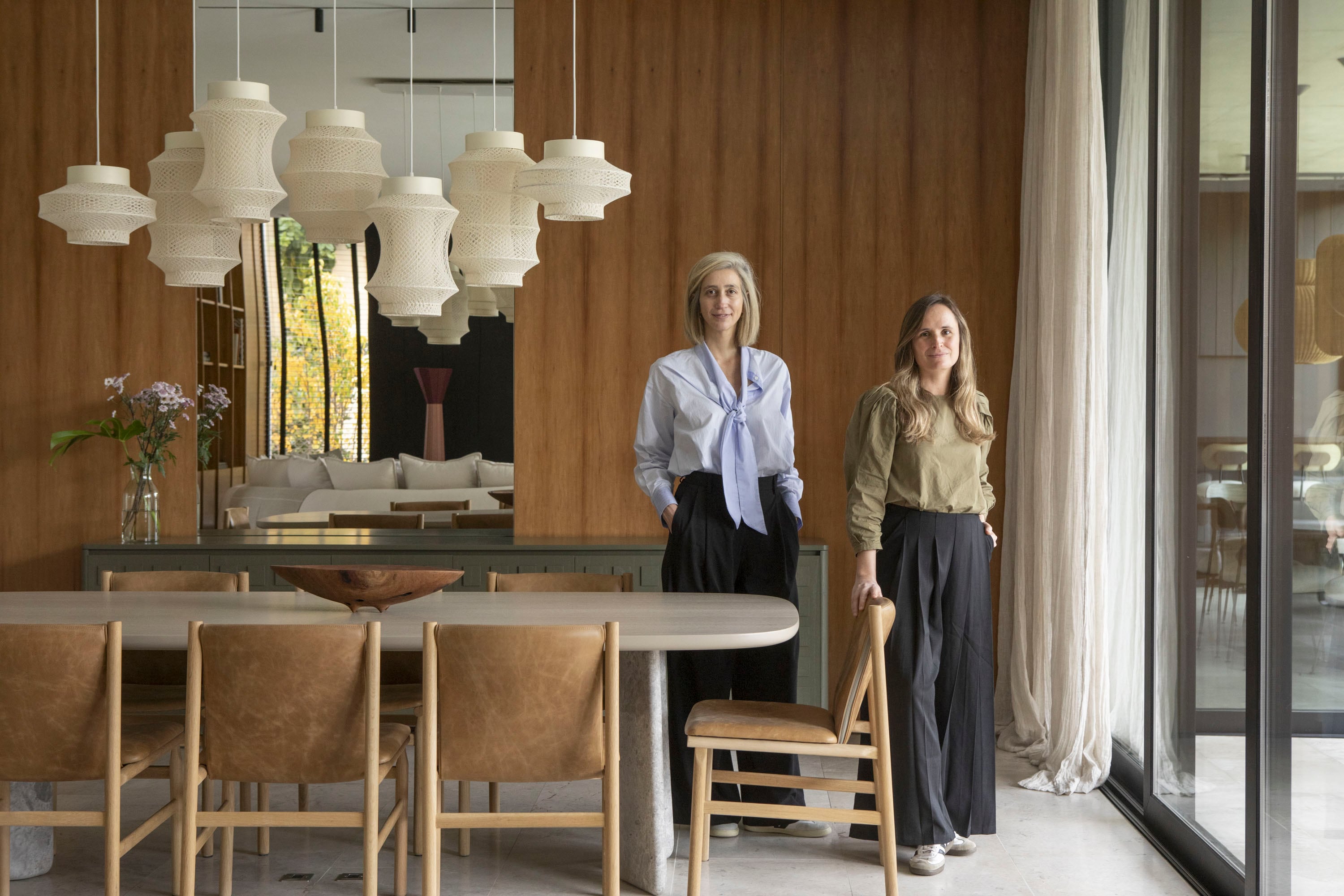 Carola Moris (izq.) y Patricia Mezzadra, responsables del diseño interior, posan en el comedor, donde una franja de espejo rompe la uniformidad del revestimiento y refleja el living contiguo.