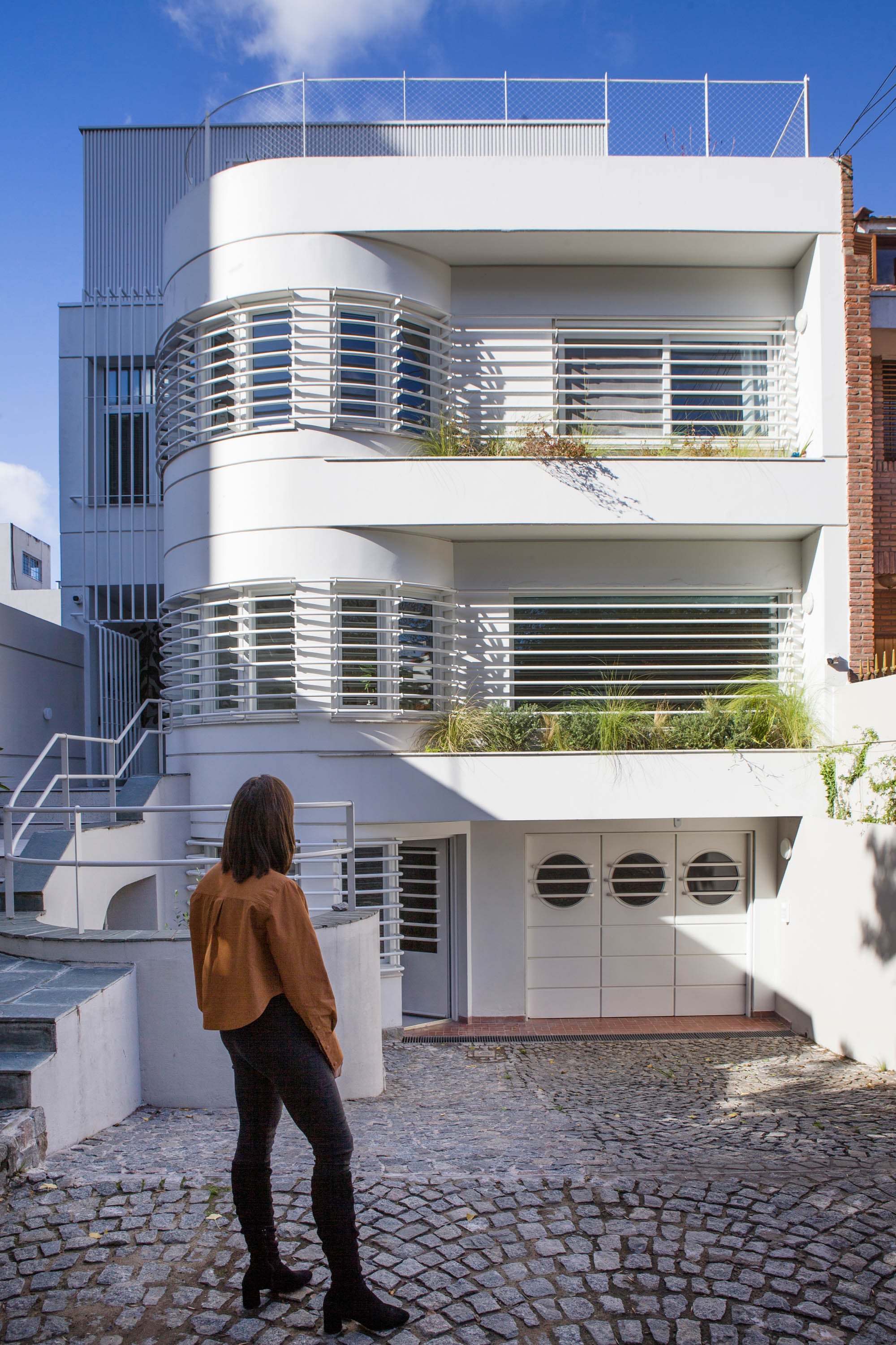 El frente muestra el garage con tres puertas con ojos de buey; el primer piso, donde está la puerta de entrada a la que se llega por la escalera lateral. El segundo piso tiene los dormitorios y, arriba de todo, están los nuevos estudios de los dueños de casa.
