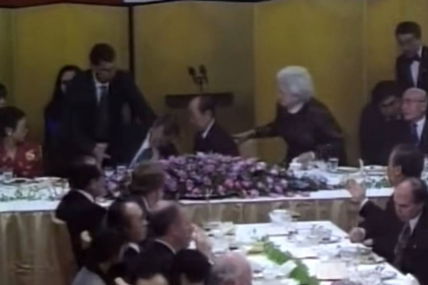 George H. W. Bush se desvanece en una cena de gala en Japón, un hecho que alarma al primer ministro nipón, Kiichi Miyazawa y la primera dama estadounidense, Barbara Bush