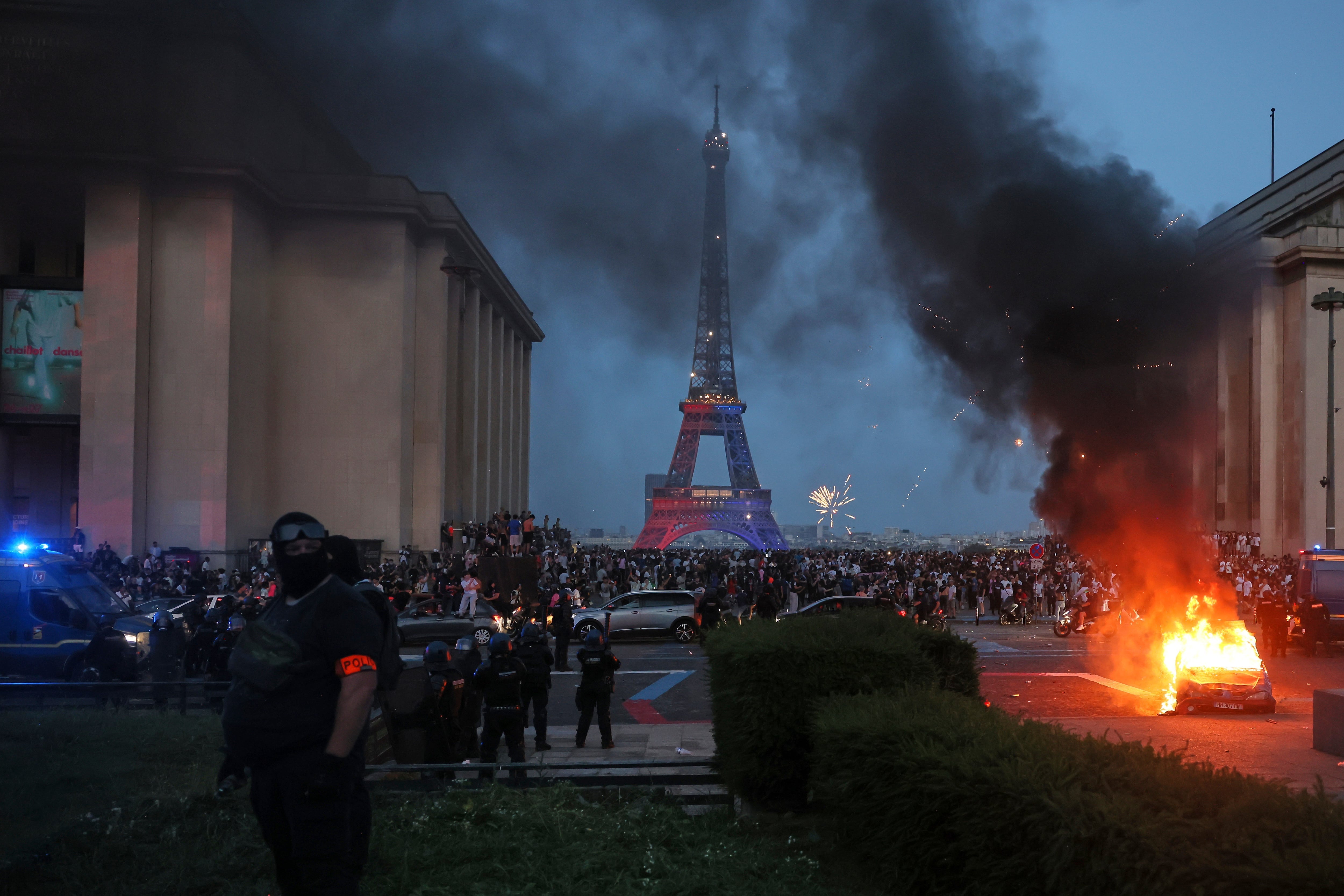 Un coche arde y estallan fuegos artificiales mientras la policía observa a los hinchas del PSG celebrar en París