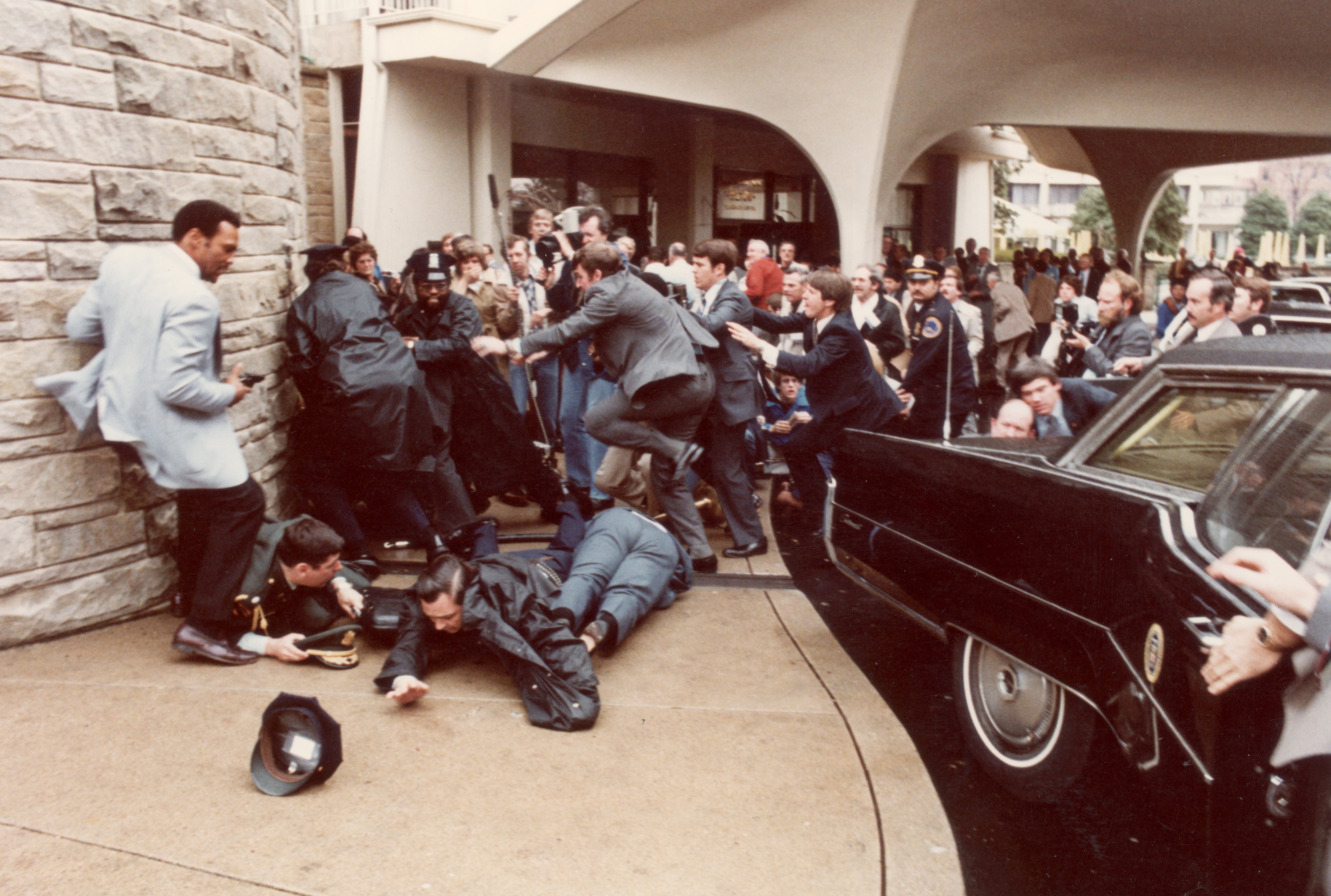 Agentes de policía y del Servicio Secreto se lanzan para proteger a Ronald Reagan en medio de una multitud aterrorizada durante el intento de asesinato