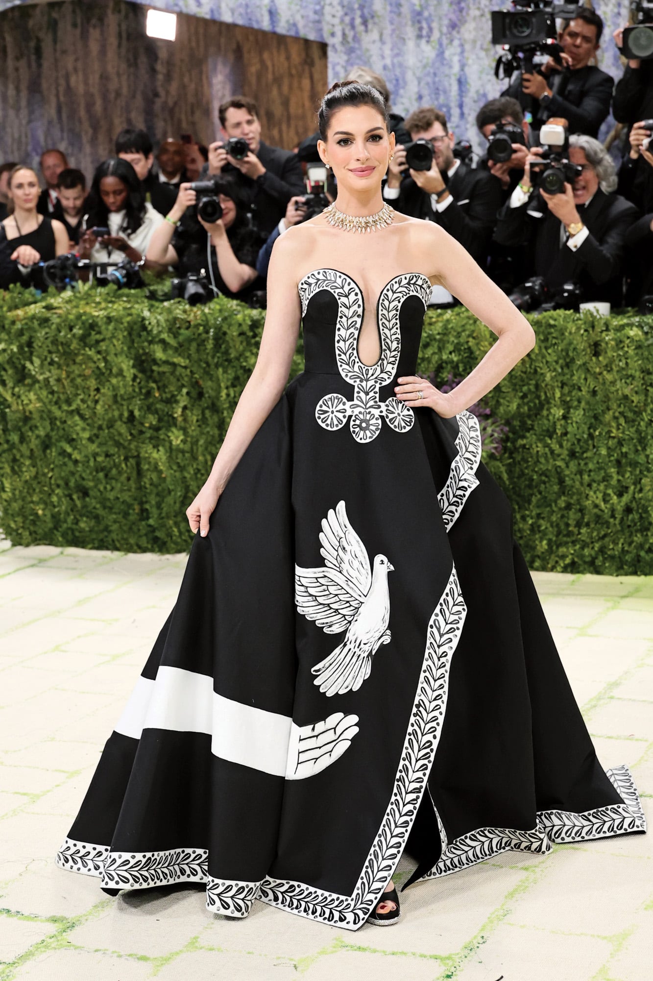 Anne Hathaway eligió un diseño en seda mikado de Michael Kors en colaboración con el artista Peter McGough, que intervino la falda con
flores, palomas y detalles de la Grecia clásica.
Está inspirado en el poema Oda a una urna griega, de John Keats