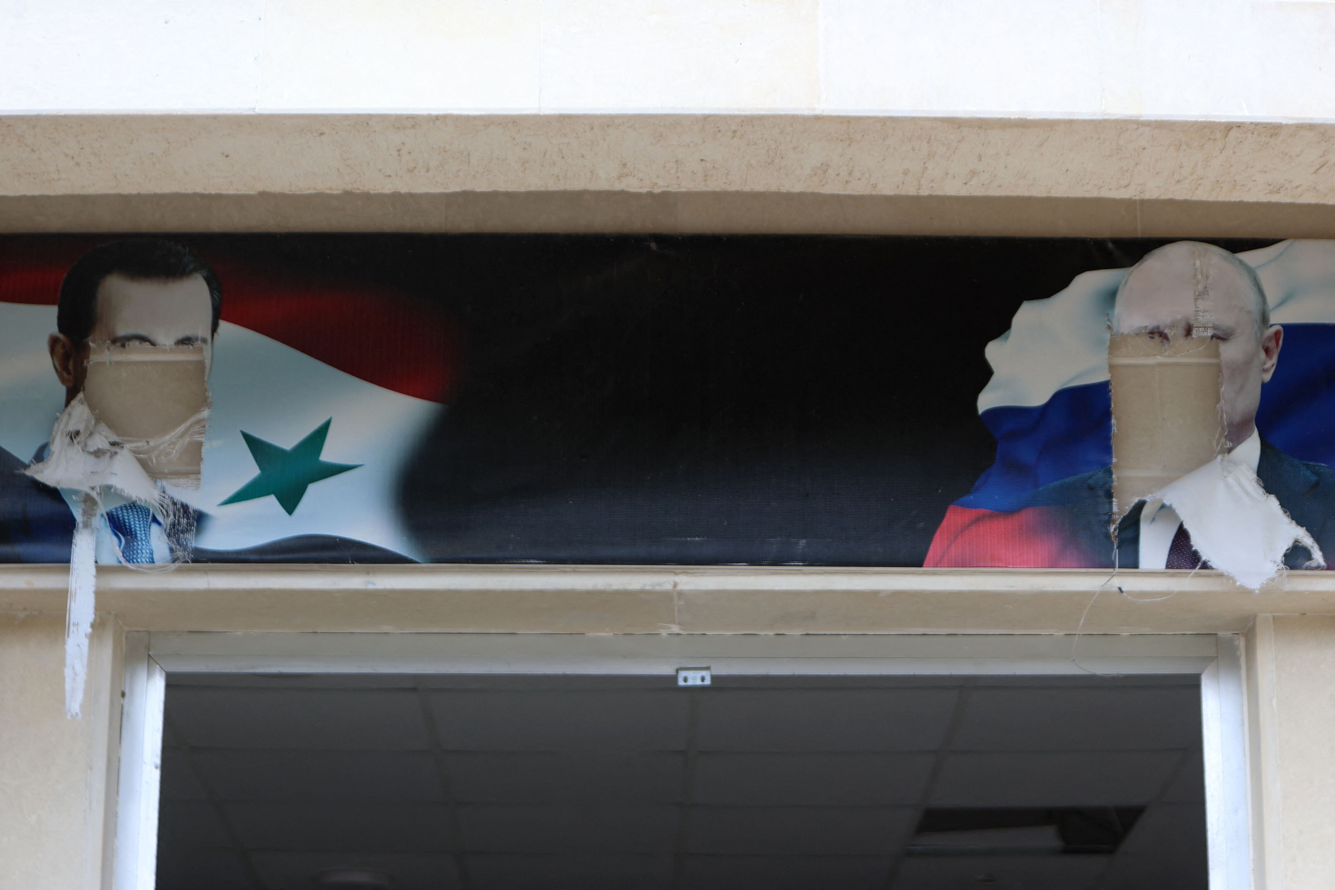 Los retratos desfigurados del derrocado presidente sirio, Bashar al-Assad, y del presidente ruso, Vladimir Putin, cuelgan sobre la entrada de un edificio, supuestamente utilizado por el ejército ruso, en la ciudad siria de Al-Bassah, en la provincia de Latakia, el 12 de diciembre de 2024. (AAREF WATAD / AFP)