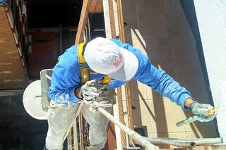 La vida desde arriba. El trabajo de pintar edificios en una silleta de madera