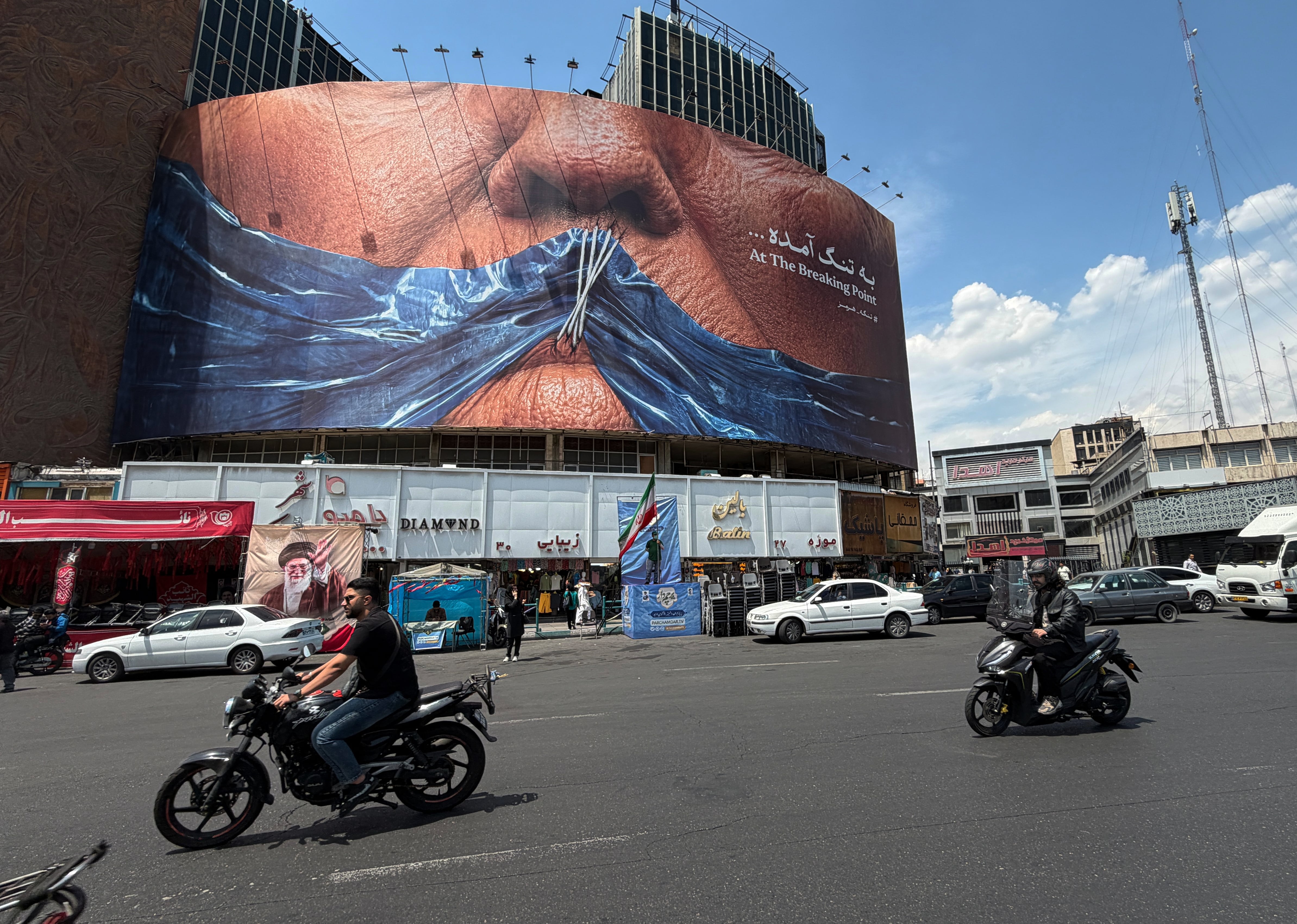 Vehículos circulan junto a una valla publicitaria con una imagen del estrecho de Ormuz y los labios cosidos del presidente estadounidense Donald Trump, en una plaza del centro de Teherán, Irán