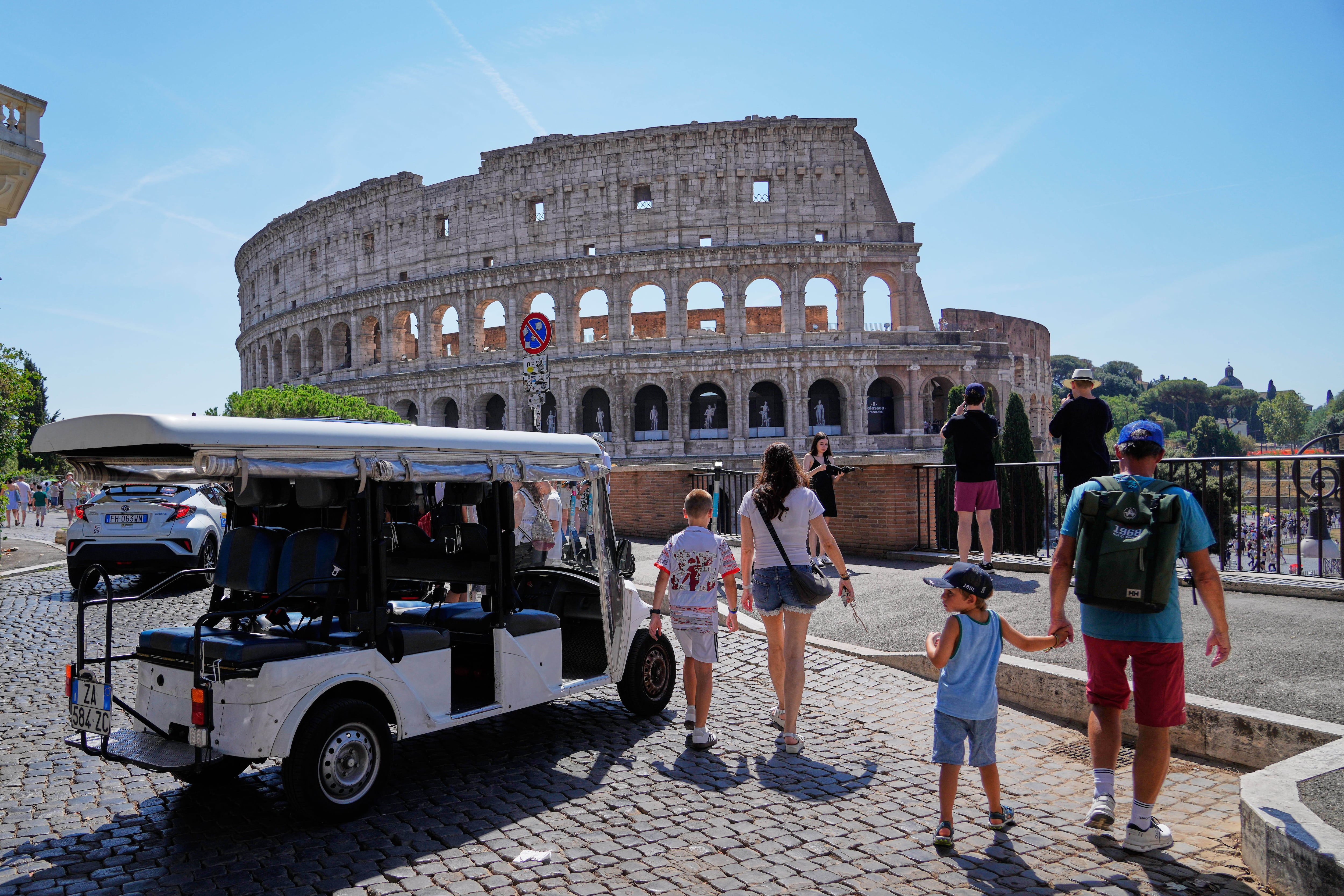 Un carrito de golf cerca del Coliseo, mientras varios turistas recorren las calles circundantes, en Roma