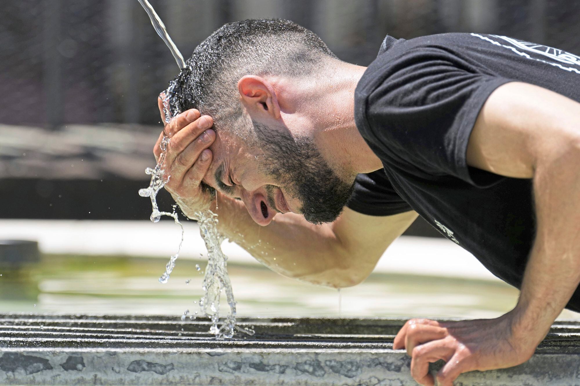 Un trabajador se refresca en una fuente durante una ola de calor en el centro de Basilea, Suiza