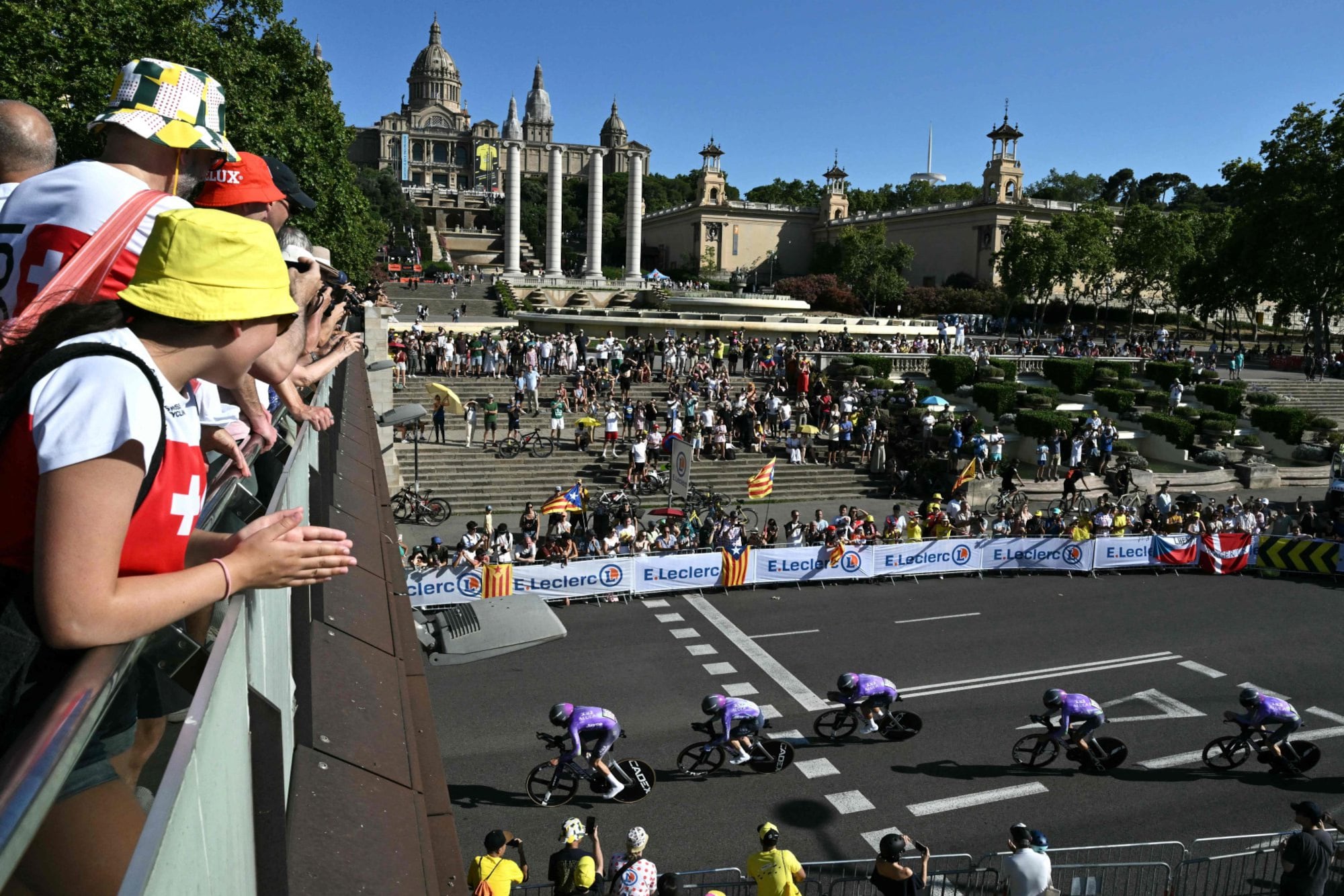El equipo Team Jayco AlUla pedalea junto al Palacio Nacional, en la colina de Montjuïc, durante la primera etapa gozada por el público, que observó a los pedalistas alrededor del circuito.
