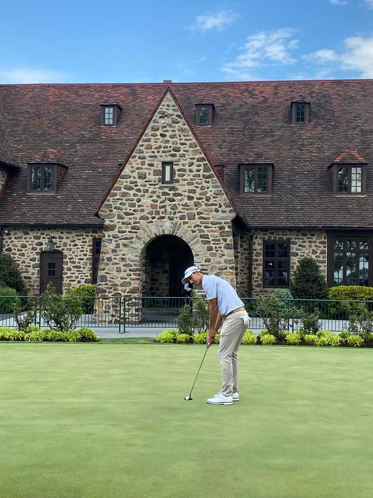 Bide practica en el putting green del Aranomink Golf Club; detrás el tradicional Club House
