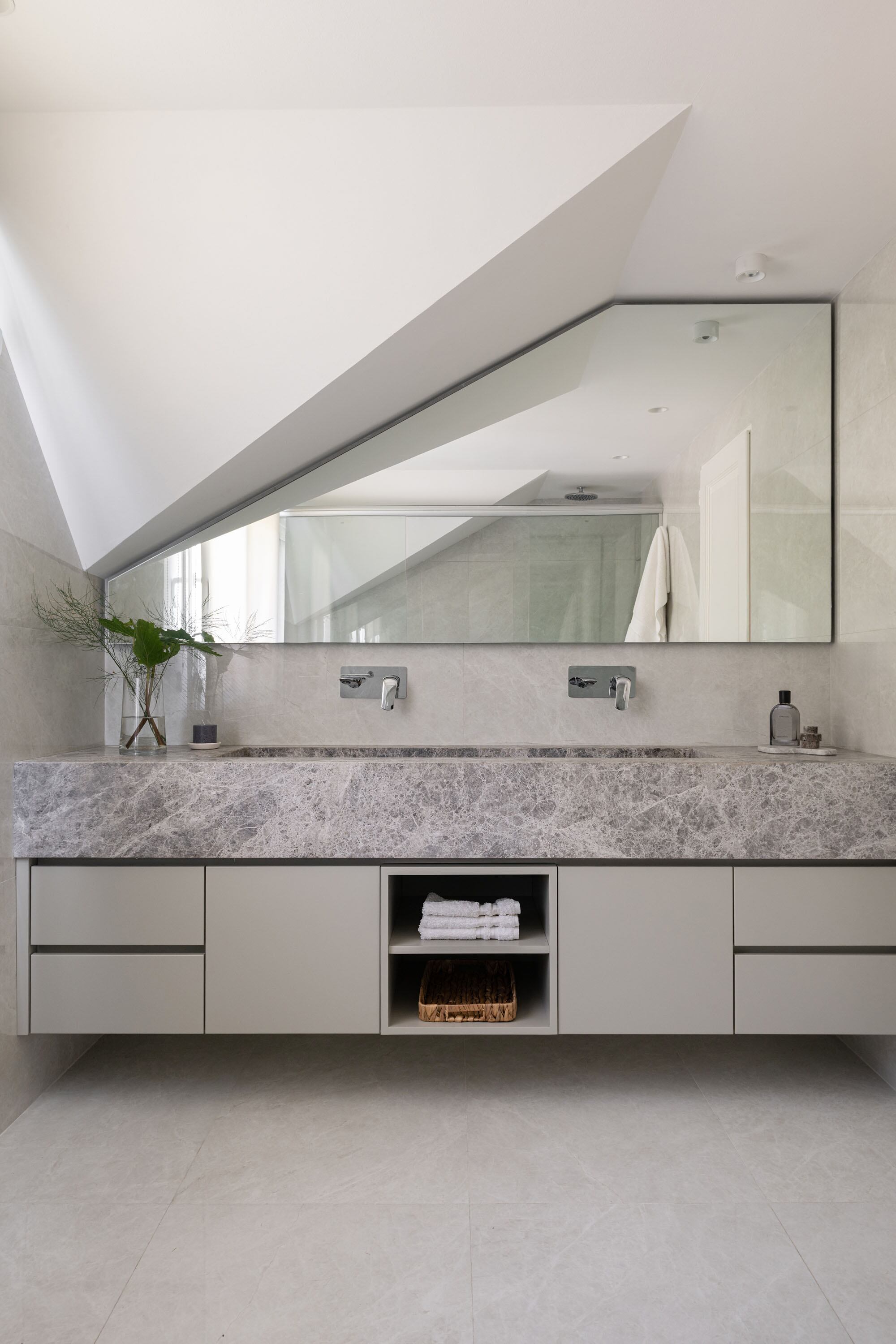 El baño conecta hacia la derecha con el vestidor. Mesada (Tundra Grey), mobiliario laqueado en gris claro, espejo a medida para acompañar la caída del techo.