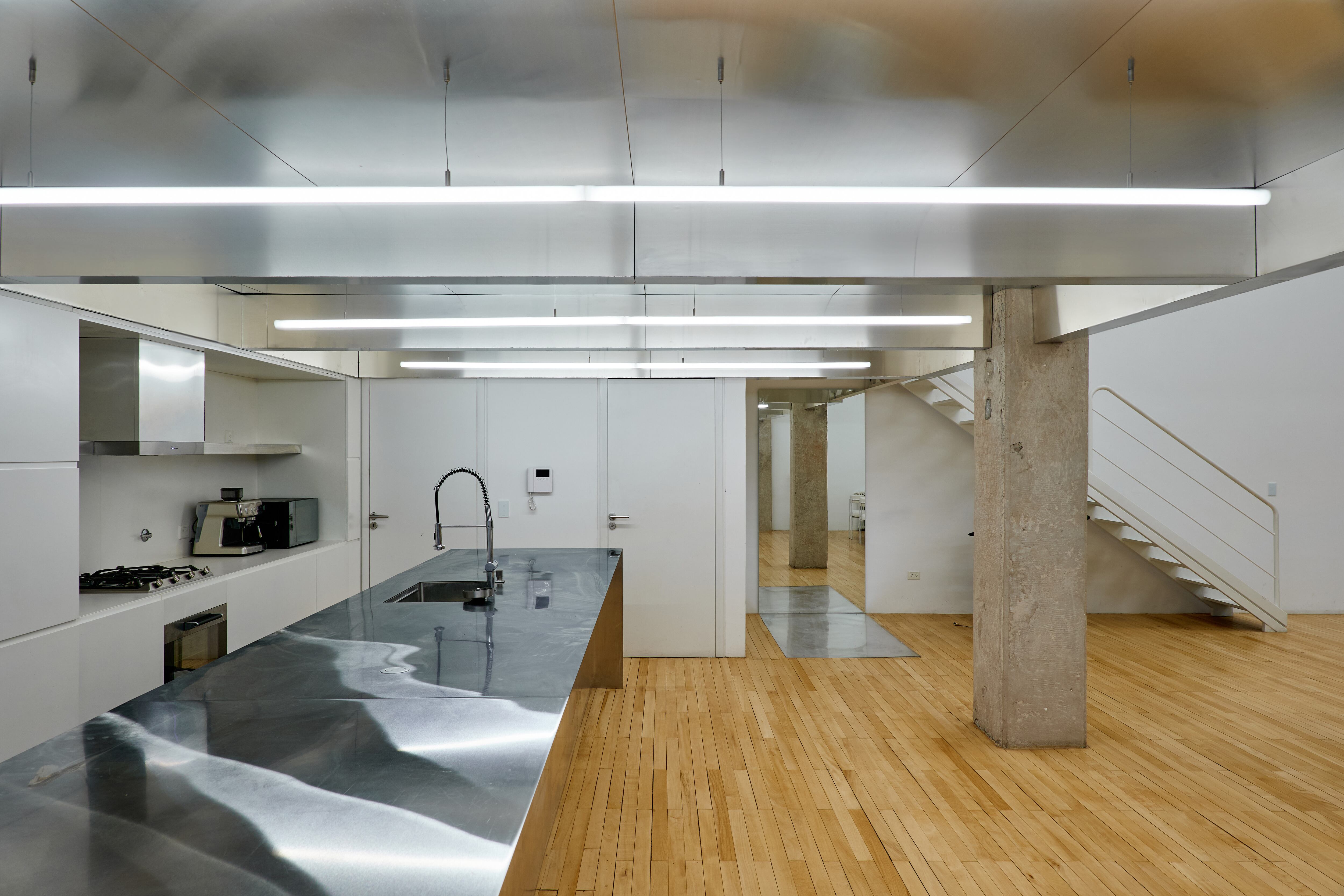 El cielorraso de la cocina mantiene el mismo ritmo de vigas que en el resto del ambiente. Lámparas de 3 metros (Huup). Mueble con nicho y mesada de Neolith. La mesada de la isla es de acero.
