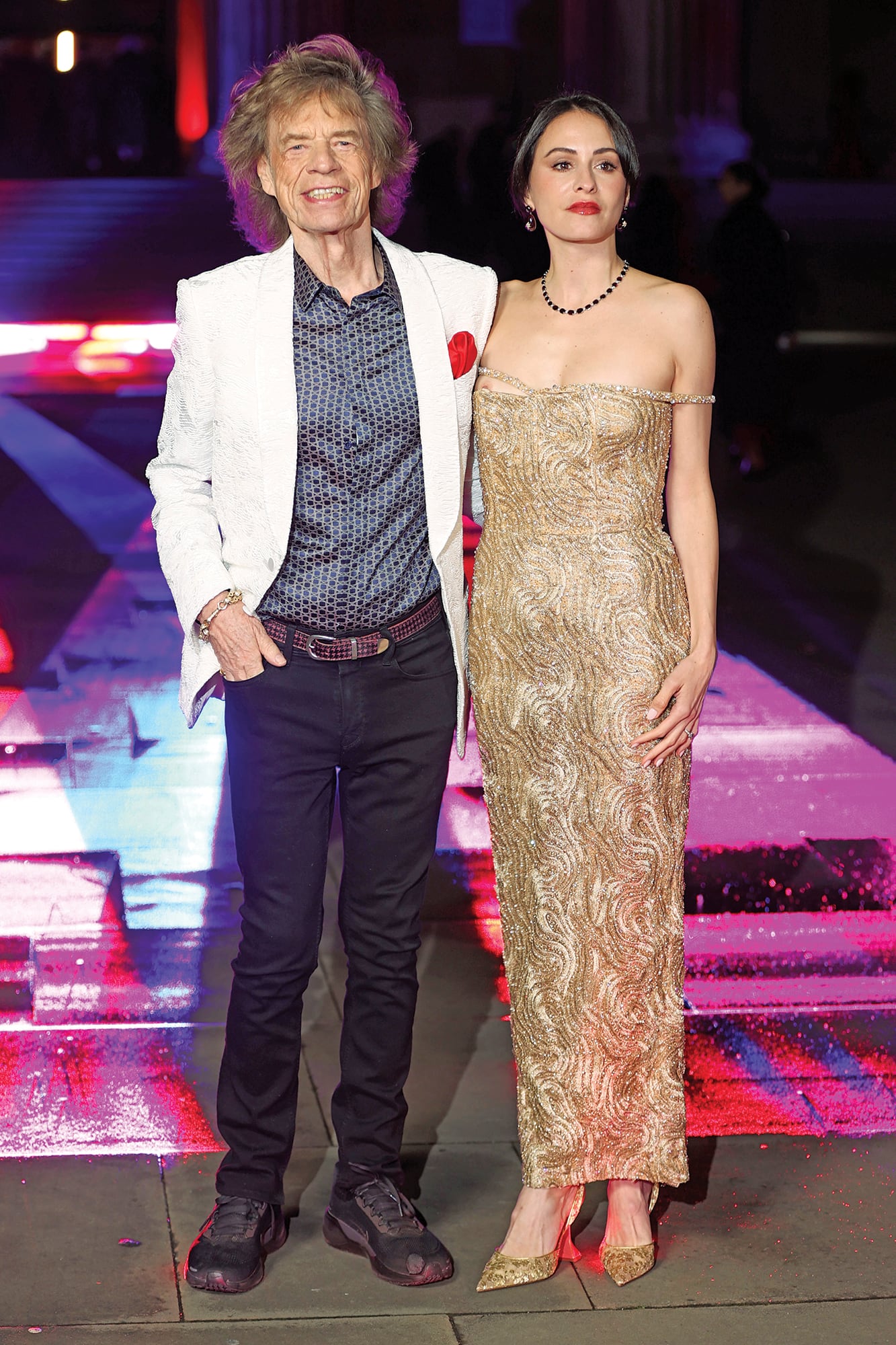 Mick Jagger apostó por un saco blanco –con un detalle rojo en la solapa– y camisa estampada. A su lado, Melanie Hamrick deslumbró con un vestido bordado en tonos dorados, pendientes y collar de piedras