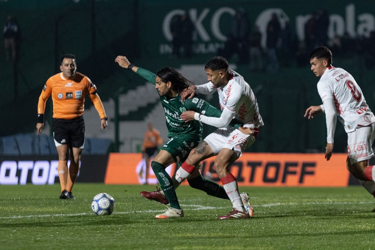 Magnín aguanta la pelota ante la marca de Godoy; sigue la acción de cerca del árbitro Lobo Medina