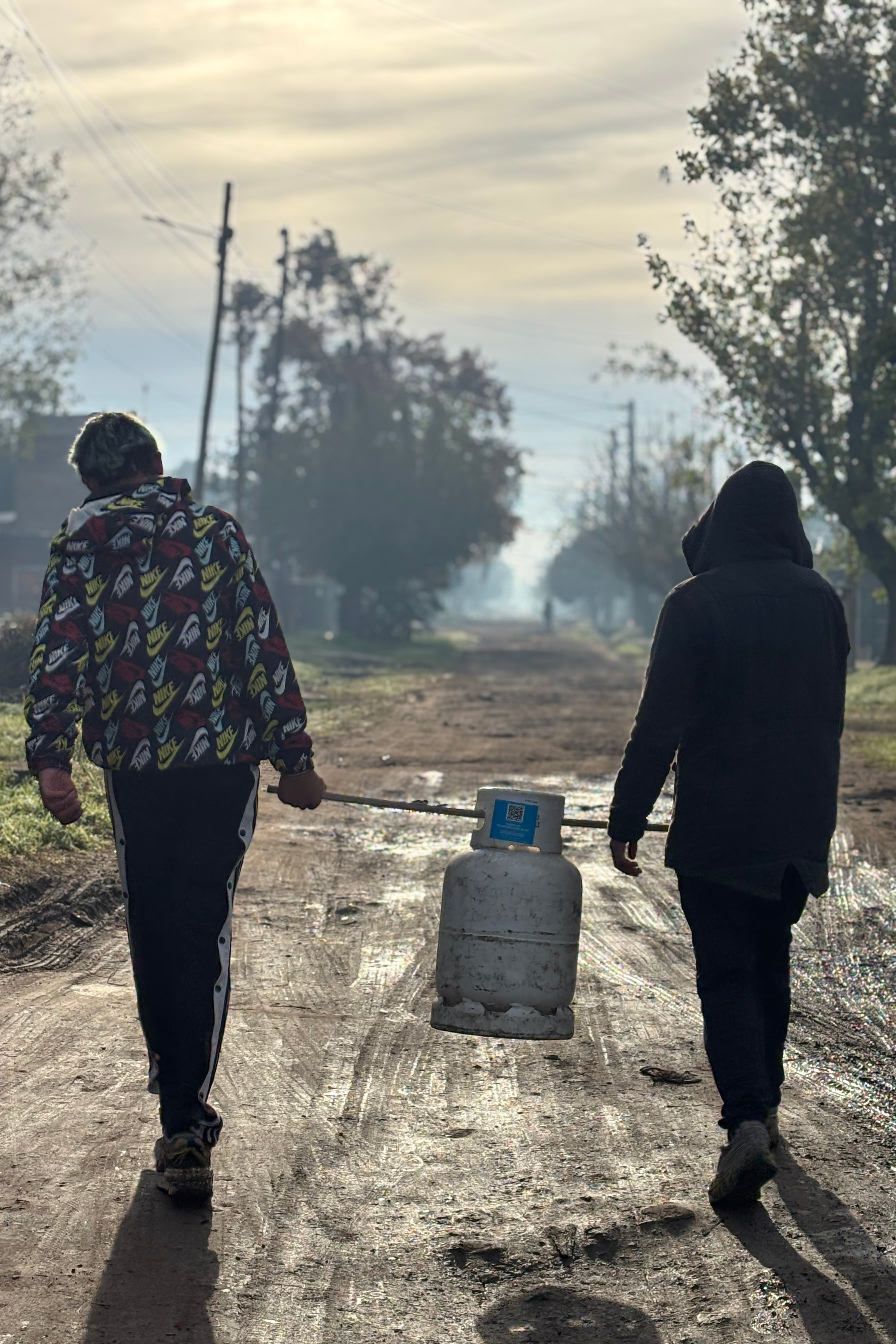 Foto registrada por @ailinbasualdo donde se ve a dos jóvenes unidos por una rama con la que se ayudan para cargar una garrafa