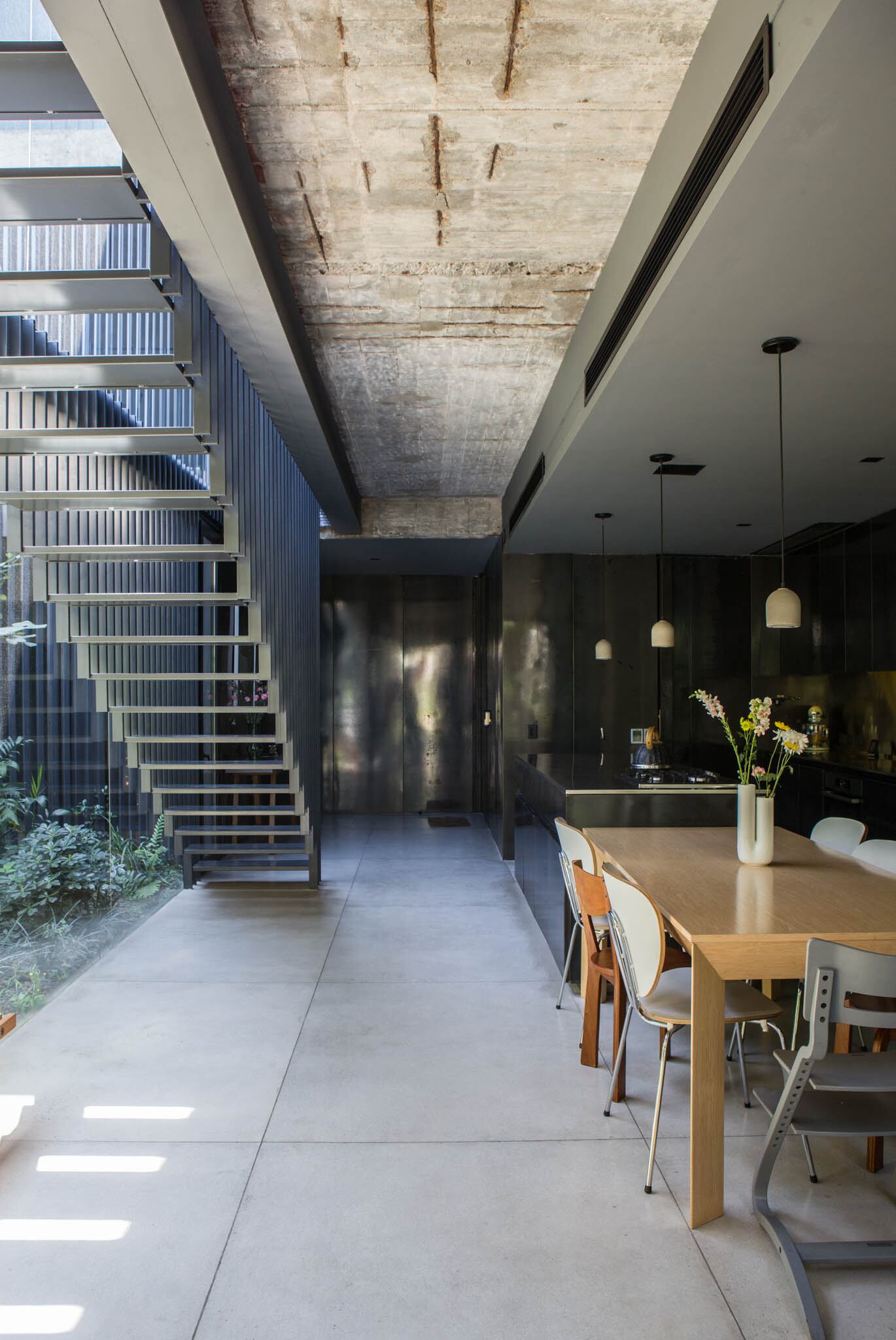 Escalera colgante de hierro (WoodHead Studio). Mesa de comedor (Gabriel García Cabrera) rodeada de distintas sillas de diseño. En la cabecera, el clásico modelo infantil de Stokke
