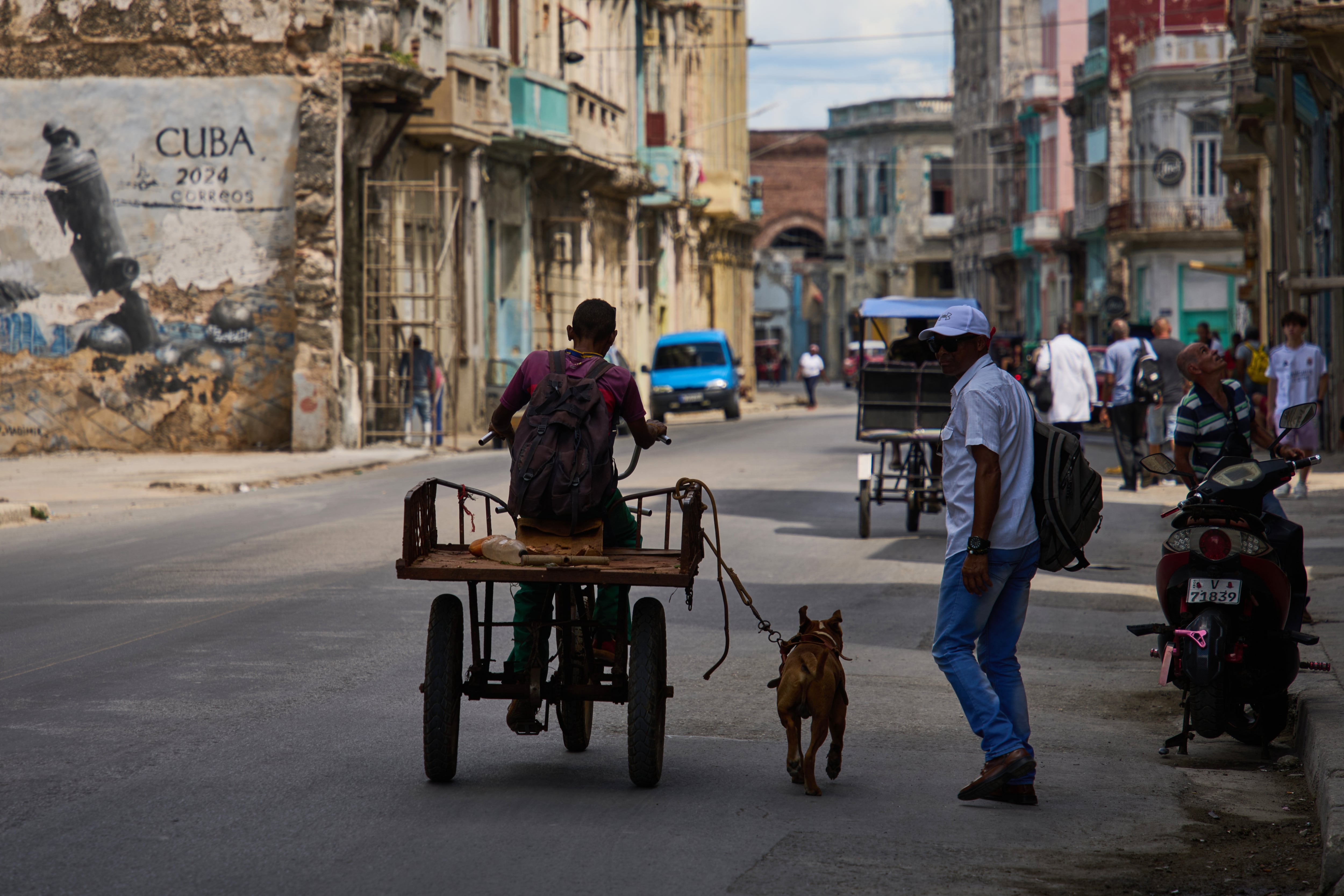 Un hombre monta en triciclo con su perro atado con correa corriendo a su lado durante un apagón en La Habana, Cuba, el lunes 16 de marzo de 2026. (Foto AP/Ramón Espinosa)