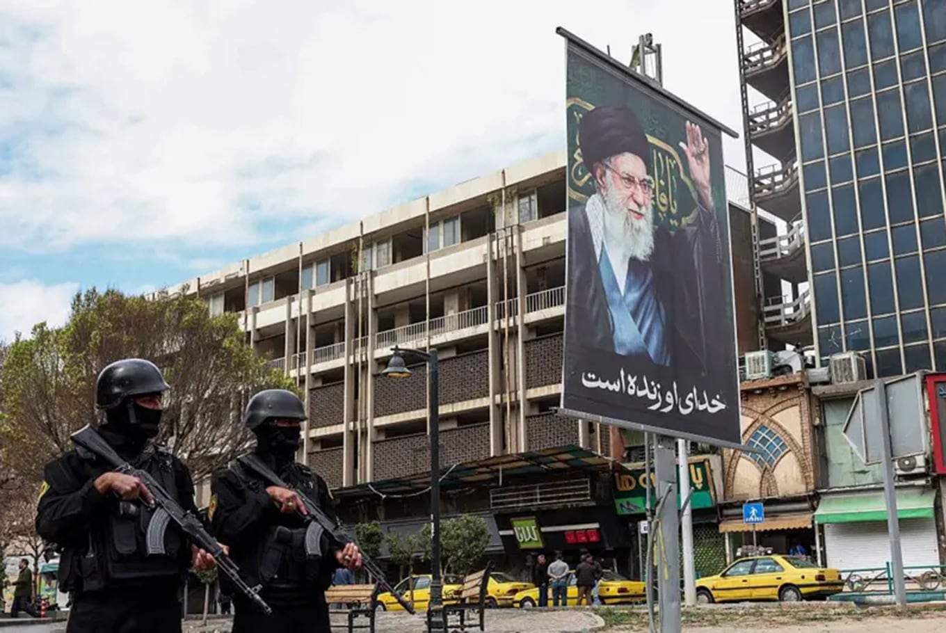 Miembros de las fuerzas de seguridad iraníes hacen guardia en una calle junto a una valla publicitaria del líder supremo de Irán, el ayatolá Alí Khamenei, fallecido en los primeros ataques del sábado.