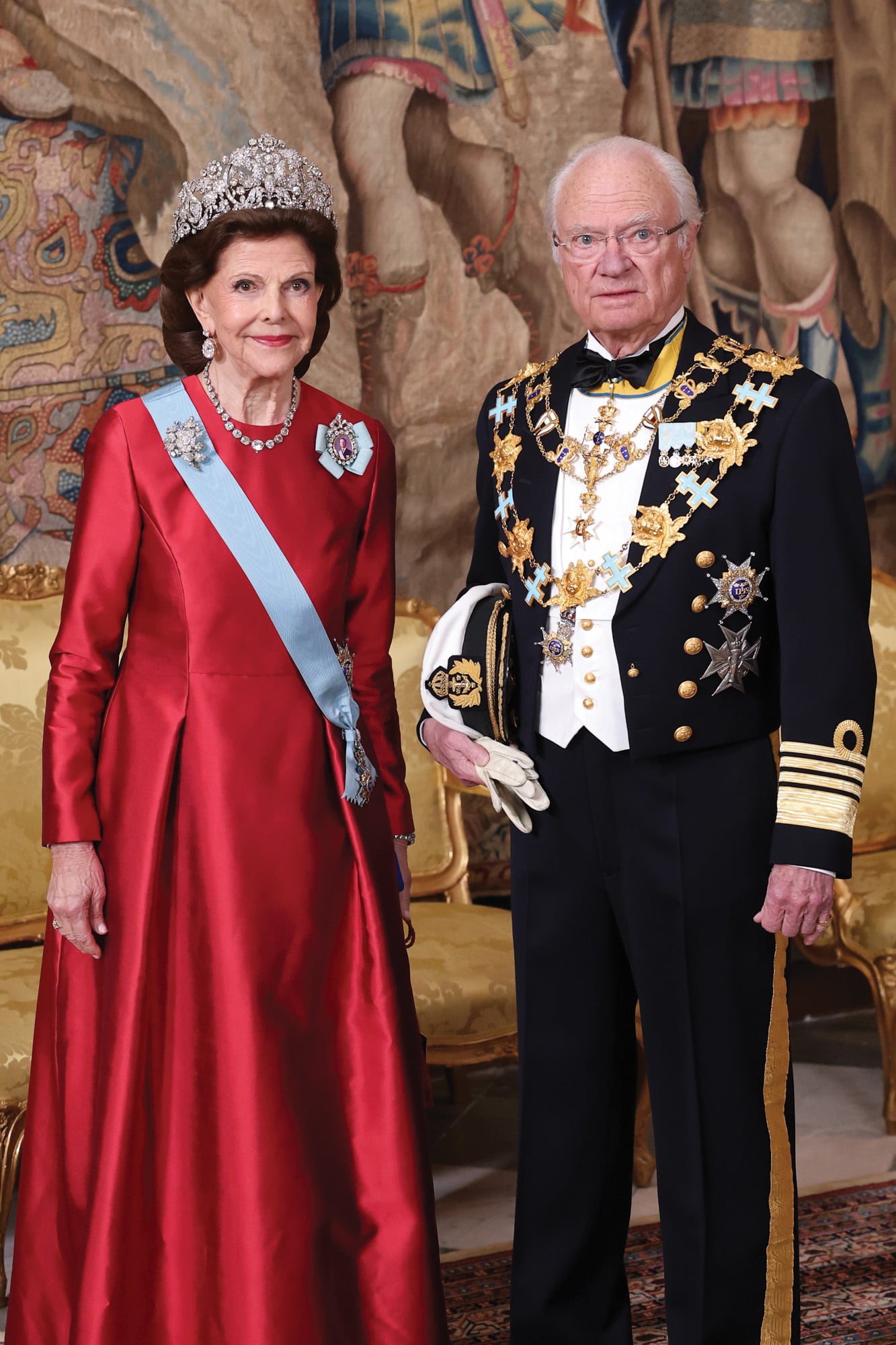 Los anfitriones, listos para recibir a sus invitados. La reina Silvia vistió un traje rojo de Georg et Arend y brilló con la tiara Braganza (elaborada con diamantes, data del siglo XIX, pesa tres kilos y es una de las más preciadas del cofre real sueco), que combinó con cadena y pendientes de diamantes y el broche rosa Braganza. También lució la banda azul claro de la Orden de los Serafines y, en su hombro izquierdo, un broche con retrato en miniatura
del rey, enmarcado en diamantes y suspendido por un lazo con los colores de la Orden de los Serafines. Su marido, el rey Carlos Gustavo, de uniforme militar y con sus condecoraciones: la Orden de los Serafines, la más alta de Suecia, la Orden de la Estrella Polar y la Orden de la Espada