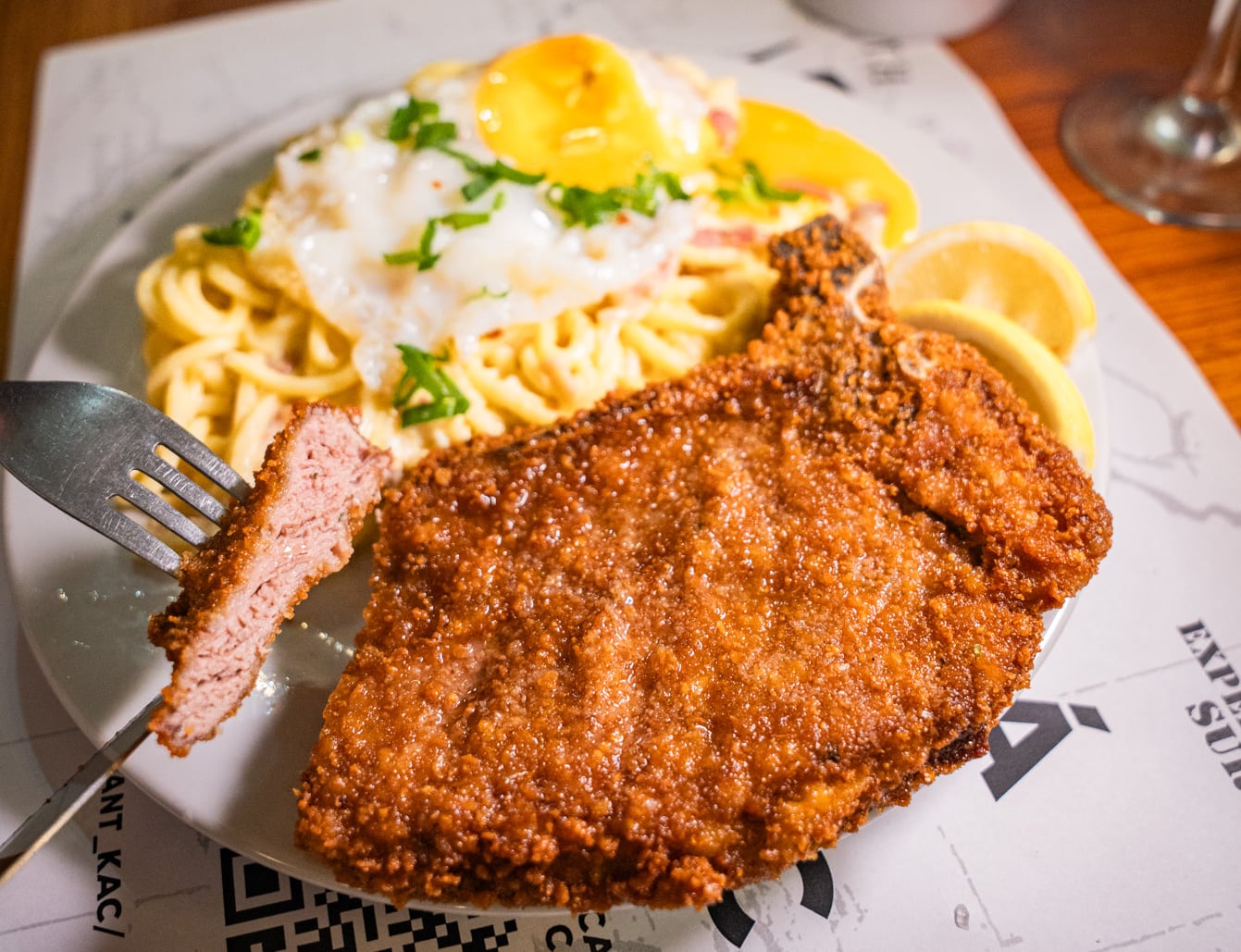 Milanesa con hueso, servida con fideos a la carbonara y huevo jugoso