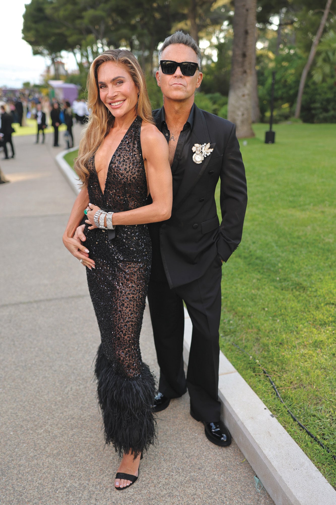 Robbie Williams y su mujer, Ayda Field, apostaron por looks coordinados cromáticamente; él con traje y camisa oscura, y ella con brillos, transparencias y plumas
