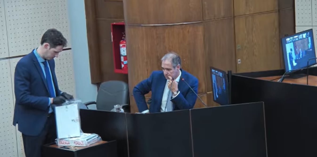 Un secretario del tribunal le exhibe los cuadernos originales al periodista