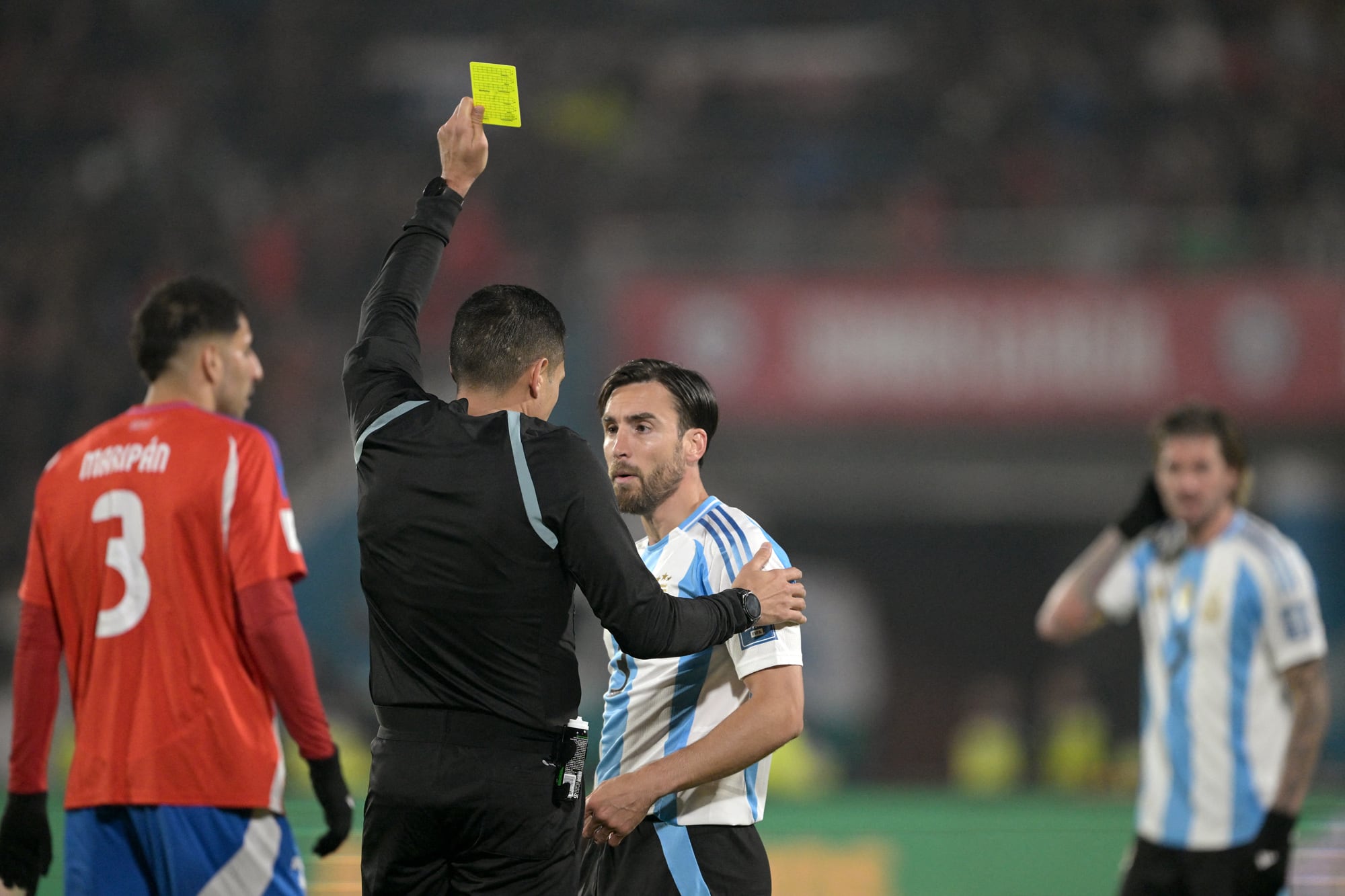 El árbitro venezolano Jesús Valenzuela muestra una tarjeta amarilla al defensor argentino Nicolás Tagliafico durante el partido de fútbol de las eliminatorias sudamericanas de la Copa Mundial de la FIFA 2026 entre Chile y Argentina
