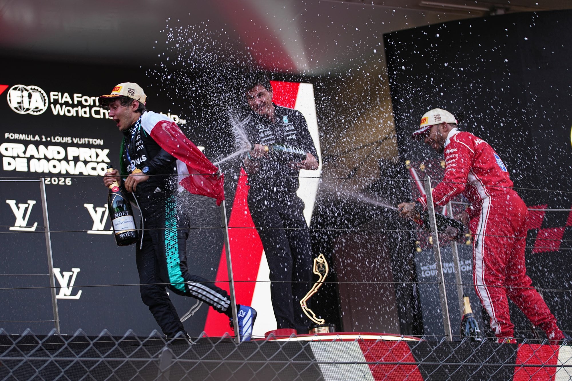 En el podio del Gran Premio de Mónaco, Andrea Kimi Antonelli no logra escapar de la lluvia de champagne que lanzan Toto Wolff y Lewis Hamilton; una celebración con pilotos del pasado y el presente de Mercedes