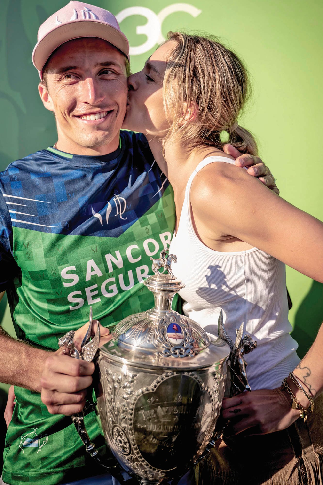 Mientras sostiene el trofeo, Barto recibe el beso de su novia, Chule