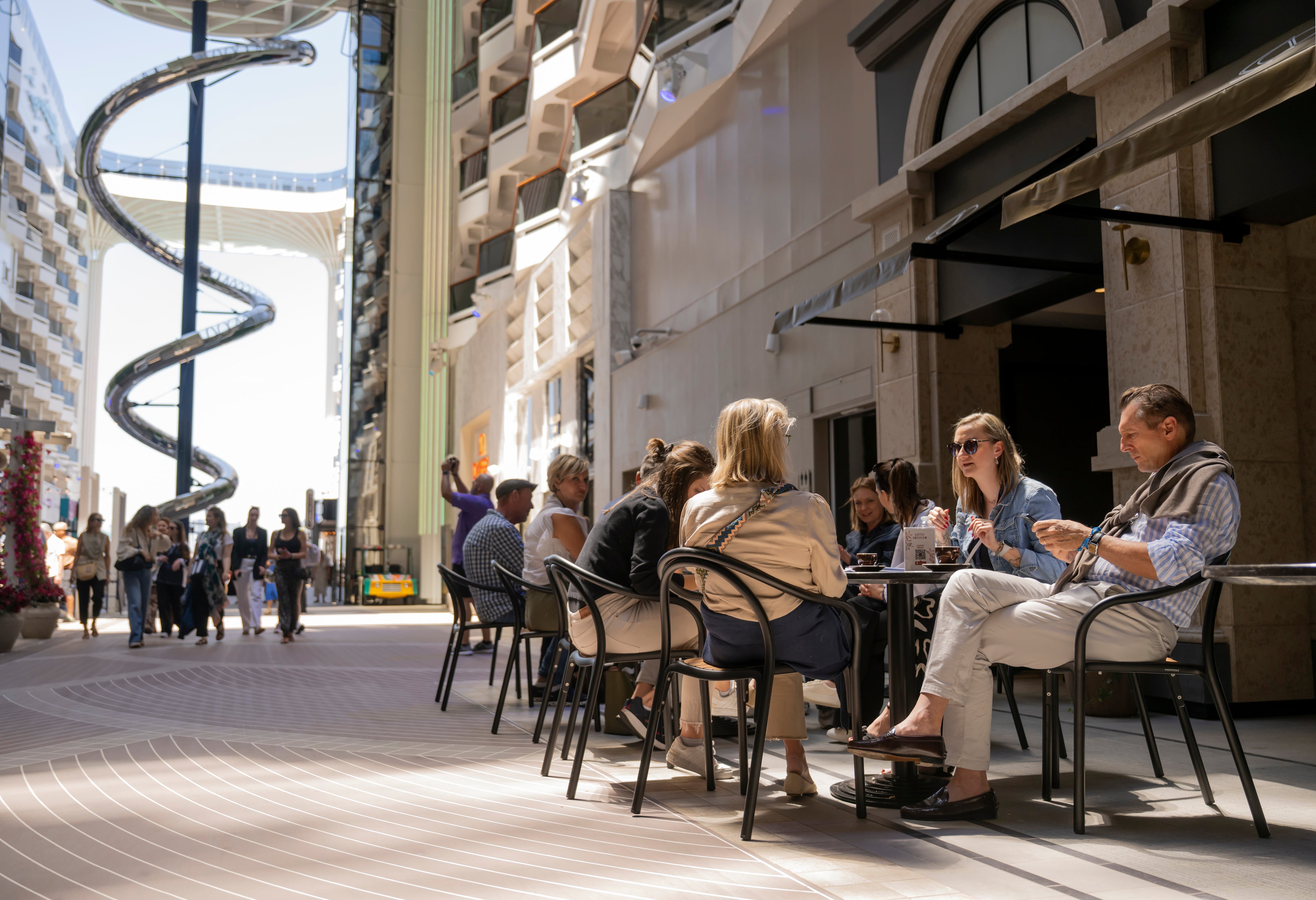 Huéspedes disfrutan de bebidas en el Coffee Emporium en el World Promenade, a bordo del nuevo barco