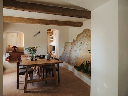 A continuación del living que acabamos de ver, el comedor, con fuerte presencia natural: pisos de terracota, vigas gruesas y la roca como una montaña a escala doméstica.