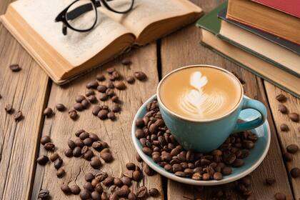 A cup of coffee with milk rests on a rustic wooden table, surrounded by coffee beans, an open book with glasses on top surrounded by books.