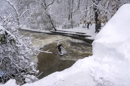 A man surfs on the Eisbach artificial river at the English Garden in Munich, Germany, Saturday, Dec. 2, 2023. Munichs airport has canceled all flights for the day after a winter storm dumped snow across southern Germany and parts of Austria and Switzerland, affecting travel across the region. Trains to and from Munichs central station were also halted, Germanys national railway said, advising passengers to delay or re-route their journeys. (Peter Kneffel/dpa via AP)
