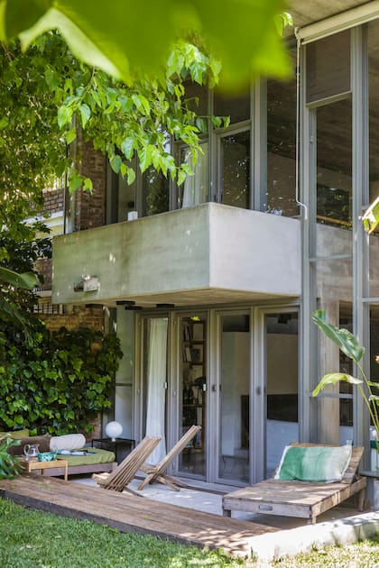 “A mí me gusta mucho la cosa bajita”, dice Gaby sobre la galería en desnivel y sus muebles”. Mesa de arrime cuadrada (La Base). Sobre la reposera de madera, almohadón verde de Ágave.