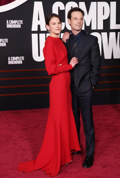 A tono con la red carpet, la actriz de Smile posó junto a su pareja Scoot McNairy con un impactante vestido rojo con cola. El actor, que en el film interpreta al músico y activista Woody Guthrie, eligió un clásico traje con camisa y corbata haciendo juego