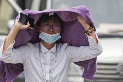 Una mujer usa un suéter para protegerse del sol mientras recorre una calle en un día caluroso en Beijing, el lunes 3 de julio de 2023