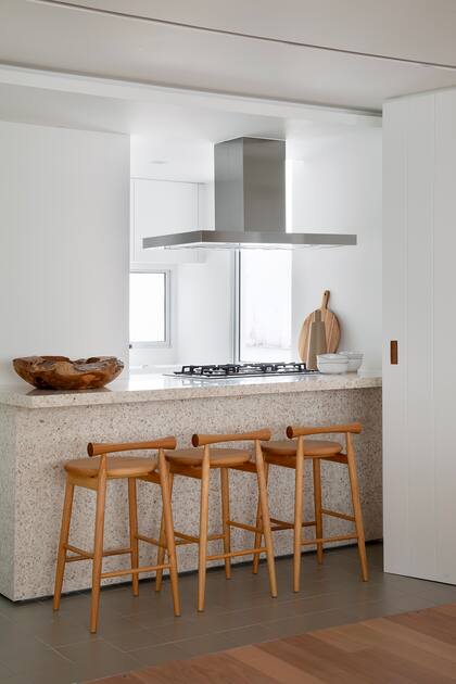 Acá el estudio propuso un juego de materialidades con pisos de cerámico, una isla de terrazo y banquetas de madera. El extractor metálico suma un contrapunto.