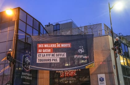 Activistas de Amnistía Internacional colocan un cartel en las oficinas de la Federación de Fútbol de Francia pidiendo que atiendan las violaciones a derechos de los trabajadores migrantes que laboran en Qatar en la preparación a la Copa Mundial el miércoles 15 de diciembre del 2021. (AP foto/Michel Euler)