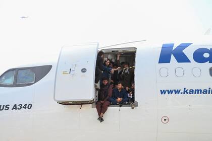 Afganos se suben a un avión y se sientan junto a la puerta mientras esperan poder escapar de los Talibanes