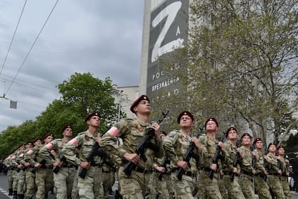 Agentes de la Guardia Nacional de Rusia marchan por una calle mientras en un edificio al fondo se ve la imagen de la letra Z, que se ha convertido en un símbolo del ejército de Rusia, el jueves 5 de mayo de 2022, en Sebastopol, Crimea