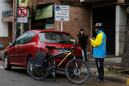 Un auto mal estacionado que está siendo infraccionado por uno de los agentes de tránsito en bicicleta