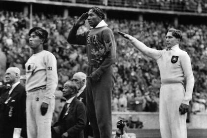 El estadounidense Jesse Owens, en el centro, durante el recibimiento de la medalla de oro después de derrotar al alemán Lutz Long, en los Juegos Olímpicos de Berlín 1936, bajo la mirada de Hitler.
