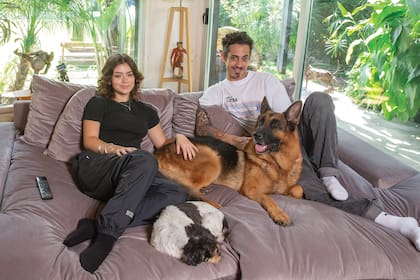 Agustín y Bianca en el enorme sillón del living, frente al televisor y con el jardín a sus espaldas. Los acompañan Honorio y Chancleta, una de las mascotas de Fer Metilli.