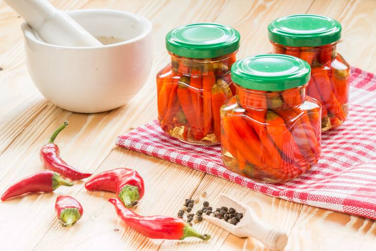 Preserved,Chili,In,Glass,Jars,On,Wooden,Table,Covered,Red