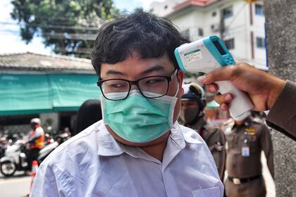 Al activista Parit "Penguin" Chirawak le toman la temperatura como medida de precaución contra la propagación del nuevo coronavirus cuando llega a la estación de policía de Nangleong en Bangkok el 25 de agosto de 2020