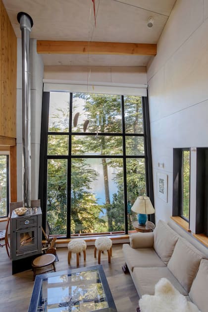 Al bajar la escalera, los ambientes se suceden como una cascada hasta que aparece la vista, imponente, tras el enorme ventanal inclinado del living.