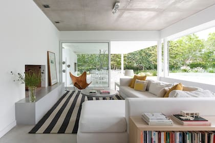 Al subir los primeros tres peldaños, se encuentra el descanso de la escalera, que se prolonga en un antepecho que recorre todo el living. El sillón en L, diseñado a medida, enmarca el sector del hogar. Alfombra a rayas (Rugit).